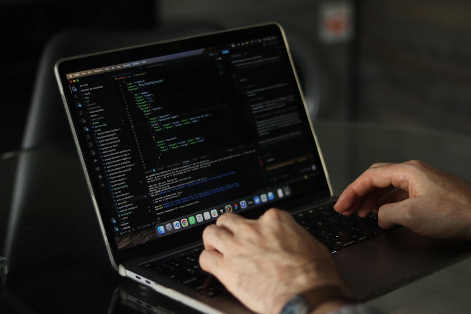 A silver laptop with a white keyboard is open on a desk, displaying lines of code on the left side of the screen and a digital calculator interface with orange buttons on the right side. The code appe